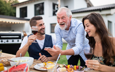 Portrait of people outdoors on family garden barbecue, using smartphone.