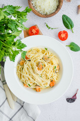 Pasta in a creamy sauce with mussels, cheese, garlic and parsley on a white plate on a light stone background. Rustic style. Vertical orientation. top view
