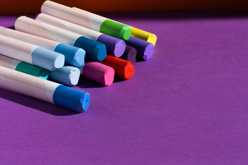 Colorful chalc pastels on purple background for copy space. Objects for creativity. Back to school concept