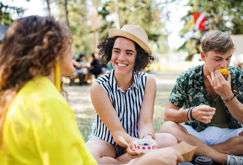 Group of young friends at summer festival, sitting on the ground and eating.