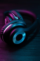 Fototapeta na wymiar Black headphone on dark wooden background. Stylish wireless headset in neon light.