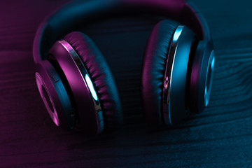 Obraz na płótnie Canvas Black headphone on dark wooden background. Stylish wireless headset in neon light.