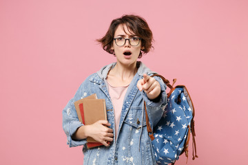 Concerned girl student in denim clothes glasses backpack isolated on pastel pink background....