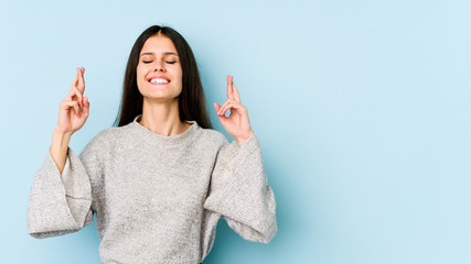 Young caucasian woman isolated on blue background crossing fingers for having luck