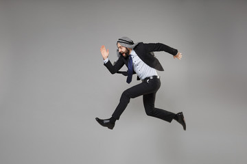 Fototapeta na wymiar Cheerful young bearded arabian muslim businessman in keffiyeh kafiya ring igal agal classic black suit isolated on gray background. Achievement career wealth business concept. Jumping like running.