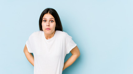 Young caucasian woman isolated on blue background shrugs shoulders and open eyes confused.