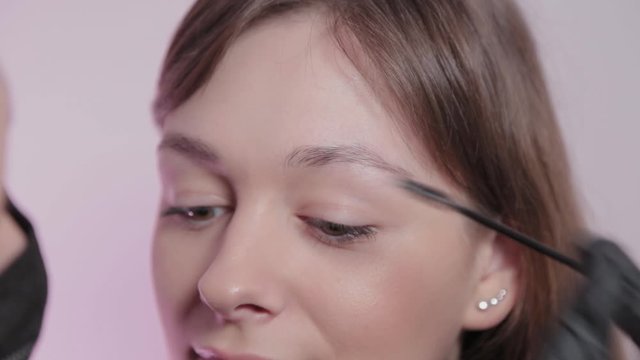 Woman master paints eyebrows to client.