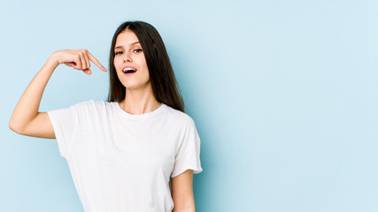 Fototapeta premium Young caucasian woman isolated on blue background person pointing by hand to a shirt copy space, proud and confident