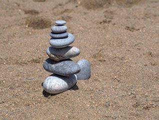 Fototapeta na wymiar A stone pyramid on fine sand made of flat and round stones. Summer calm background.