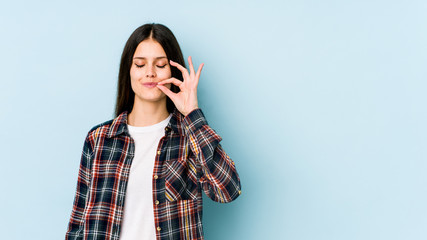 Young caucasian woman isolated on blue background with fingers on lips keeping a secret.