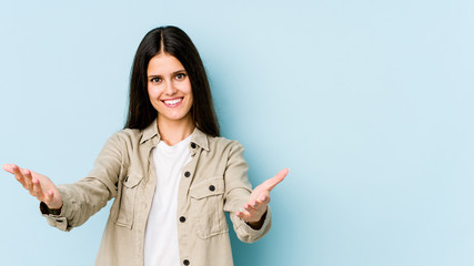 Young caucasian woman isolated on blue background showing a welcome expression.