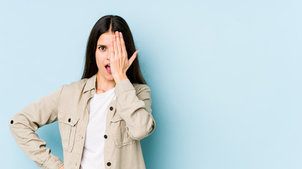 Young caucasian woman isolated on blue background having fun covering half of face with palm.