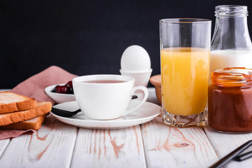 Delicious, healthy, hearty breakfast on the white table. Eggs, oatmeal, milk, tea, banana toast, homemade salted caramel, pancakes with fruit, orange juice.