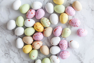 Happy Easter concept. Preparation for holiday. Easter pastel candy chocolate eggs sweets on trendy gray marble background. Simple minimalism flat lay top view copy space.