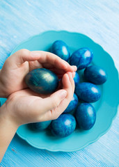 blue eggs laid out in a plate on the table for Easter. A child holds an Easter egg in his hands