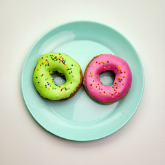 Two delicious donuts of different colors on a blue plate.