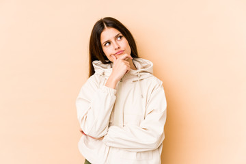 Young caucasian woman isolated on beige background thinking and looking up, being reflective, contemplating, having a fantasy.
