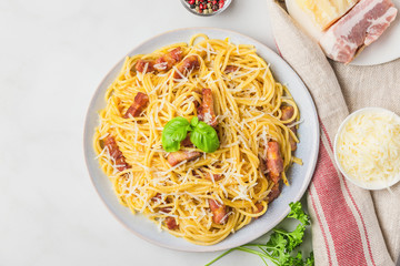 Italian pasta carbonara made of spaghetti, bacon, parmesan cheese and basil in a plate on white marble table