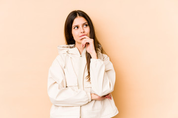 Young caucasian woman isolated on beige background relaxed thinking about something looking at a copy space.