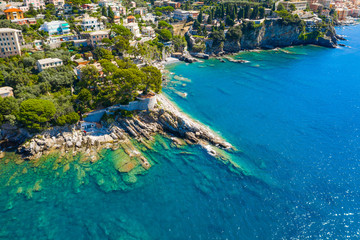 Aerial view on the city with colorful houses located on the rocky coast of ligurian sea, Camogli near Genoa, Italy. Rocky Coastline is washed by turquoise blue water.