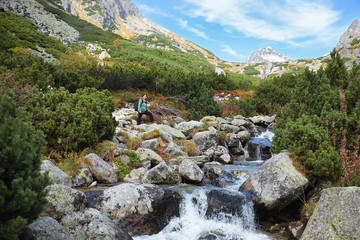 Tourist woman Standing at a mountain stream on stones with pine forest and a peak in the background. © andras_csontos