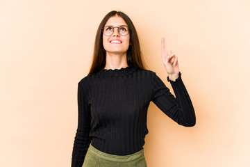 Young caucasian woman isolated on beige background indicates with both fore fingers up showing a...