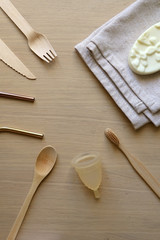Various zero waste products on a wooden table: cloth, soap, cutlery, straws, toothbrush and menstrual cup. Top view.