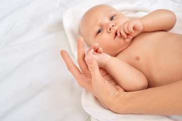 Baby Care. Young mother with little son sucking thumb curious lying on bed at home holding his little hand tender close-up