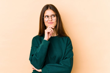 Young caucasian woman isolated on beige background looking sideways with doubtful and skeptical expression.