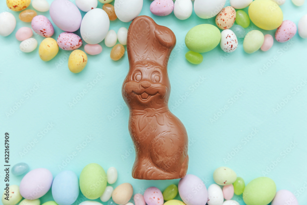 Wall mural Happy Easter concept. Preparation for holiday. Easter candy chocolate eggs bunny and jellybean sweets isolated on trendy pastel blue background. Simple minimalism flat lay top view copy space.