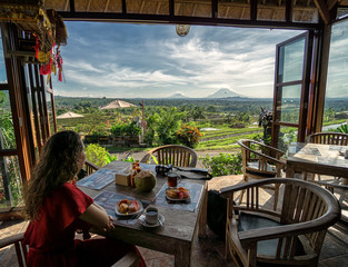Young brunette girl having breakfast with view over the Jatiluwih rice terrace from open restaurant on Bali, Indonesia 