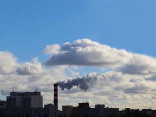 Fototapeta na wymiar A factory chimney emits clouds of smoke that are mixed with ordinary clouds. The theme of ecology and nature.