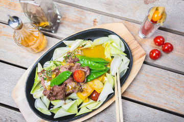 Fried pieces of meat with vegetables in a hot pan on a wooden table in a restaurant.
