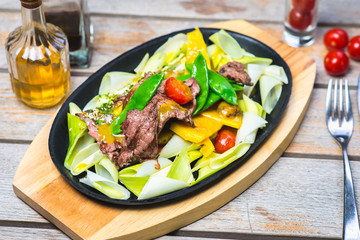 Fried pieces of meat with vegetables in a hot pan on a wooden table in a restaurant.