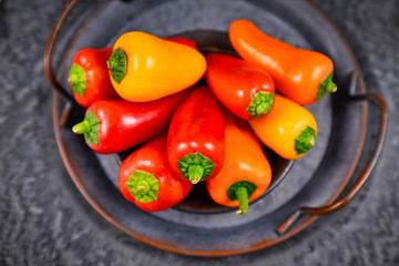 Mixture of chilli shaped red, orange and yellow capsicums pepper vegetables in bowl on dark background