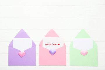Colorful paper envelopes with hearts and text With Love on white wooden table