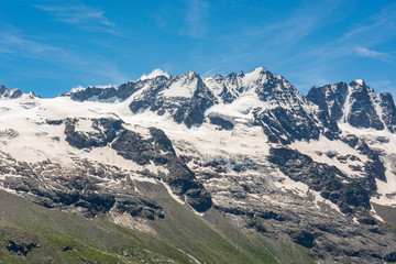 Fototapeta na wymiar Spectacular mountain panorama with peaks and slopes covered with glaciers above lush green valley.