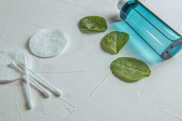 blue micellar water, green spinach leaves, cotton pads and sticks on a concrete background. with place for an inscription.