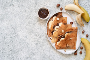 Crepes with chocolate paste, bananas and nuts on a white wooden background.