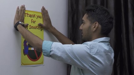 Indian man posting No smoking poster in his room. Say no to smoking & drugs. Be healthy & fit.