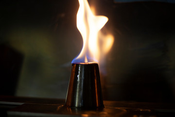 Alcohol burns on a stack for alcoholic drinks. Tongues of flame around a metal cup. Texture of fire. Yellow fire on a black background. Fire at the bar. The tradition of setting fire to alcohol.