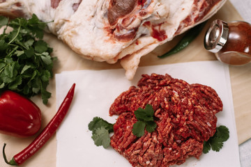 Red fresh minced meat on the background of lamb legs, red pepper and greens. Ground beef on the background of fresh meat in the kitchen of a housewife