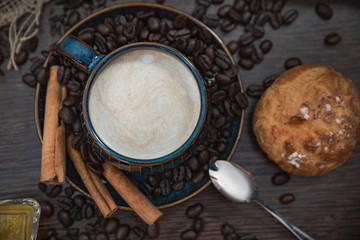 cup of coffee with cinnamon sticks and bun on brown table