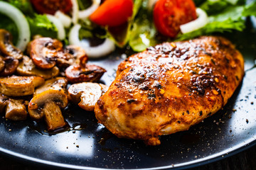 Roast chicken breast and vegetables on wooden background