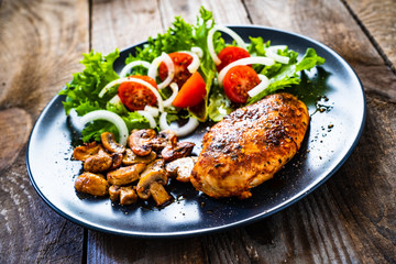 Roast chicken breast and vegetables on wooden background