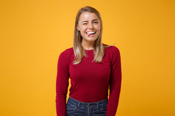 Funny young blonde woman girl in casual clothes posing isolated on yellow orange background studio portrait. People sincere emotions lifestyle concept. Mock up copy space. Blinking showing tongue.