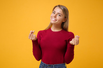 Smiling young blonde woman girl in casual clothes posing isolated on yellow orange wall background. People lifestyle concept. Mock up copy space. Rubbing fingers showing cash gesture asking for money.