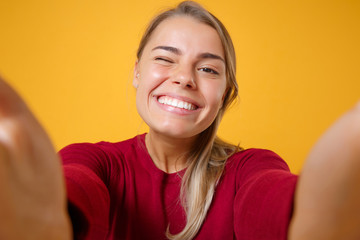 Close up of smiling young blonde woman girl in casual clothes posing isolated on yellow orange background. People lifestyle concept. Mock up copy space. Doing selfie shot on mobile phone, blinking.