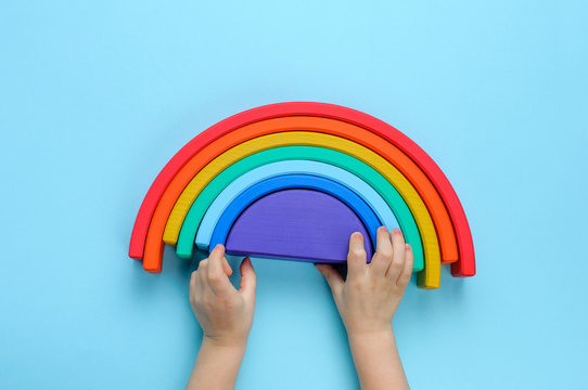 Kids hands playing with wooden toy rainbow on blue background