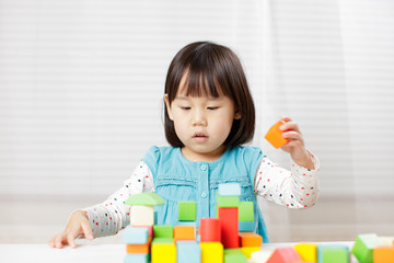 toddler girl playing creative toy blocks at home against white background